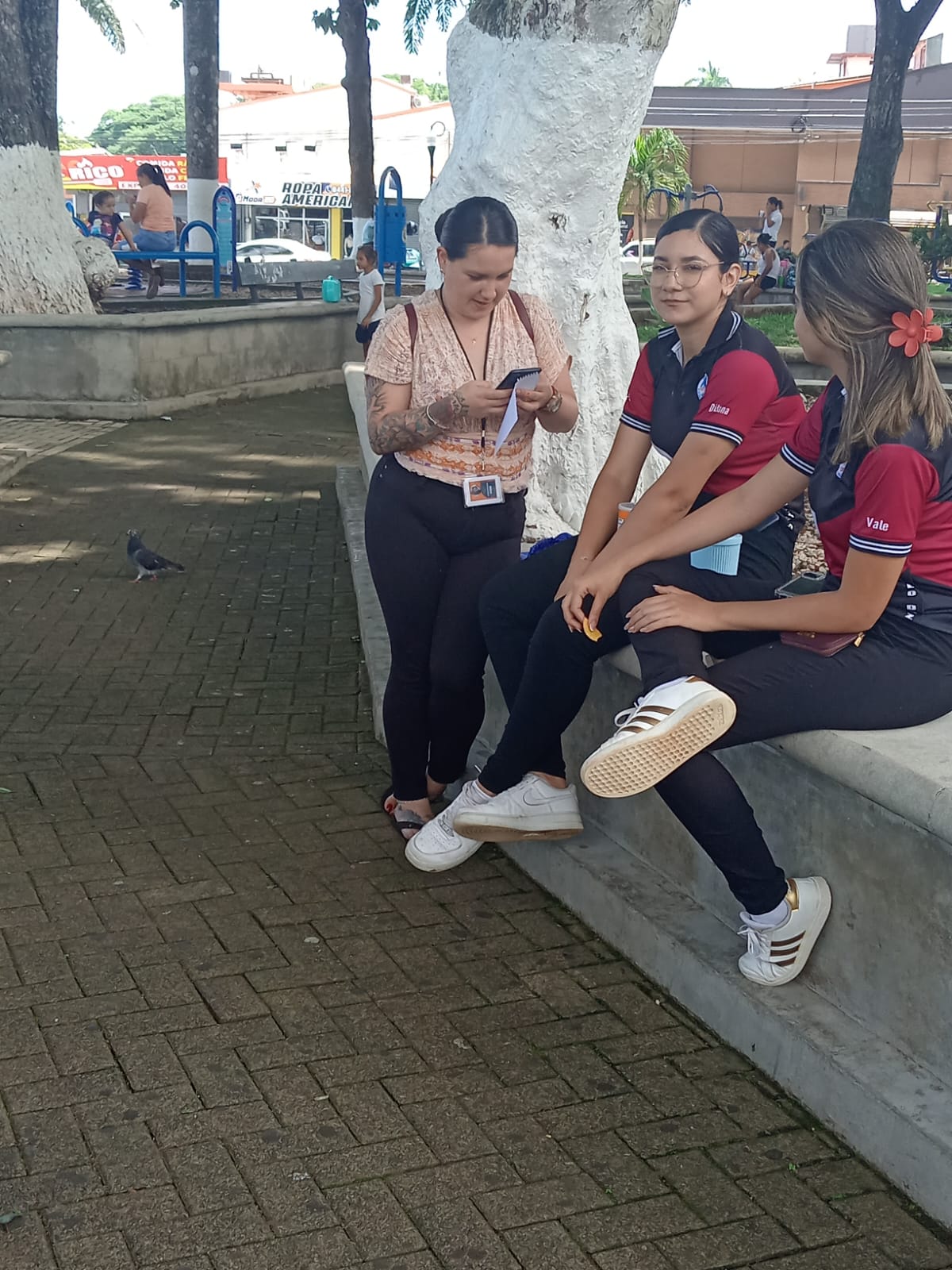 Market Research in Central America Field interviewer speaking with two people outdoors while holding a mobile device